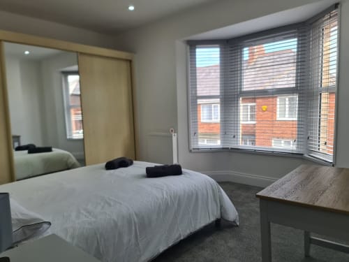 Modern bedroom at 2 Doves Holiday Property in Exeter with white bed, desk, mirror, and bay windows overlooking brick