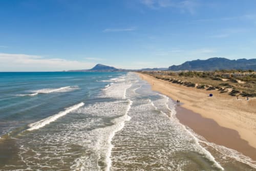 Playa de arena con olas turquesas y montañas en la costa de Ròtova, España