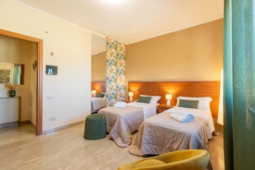 Spaziosa camera familiare a La Zagara Rooms a Milazzo con due letti, caldi accenti arancioni e comfort moderni