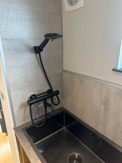 Black shower fixture with rainfall head over black basin in modern bathroom at 2 Doves Holiday Property, Exeter