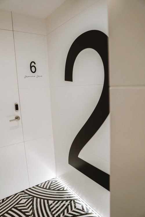 Corredor moderno del hotel Mamma Mia Tossa mostrando habitación número 6 con diseño geométrico minimalista en blanco y negro sobre azulejos blancos