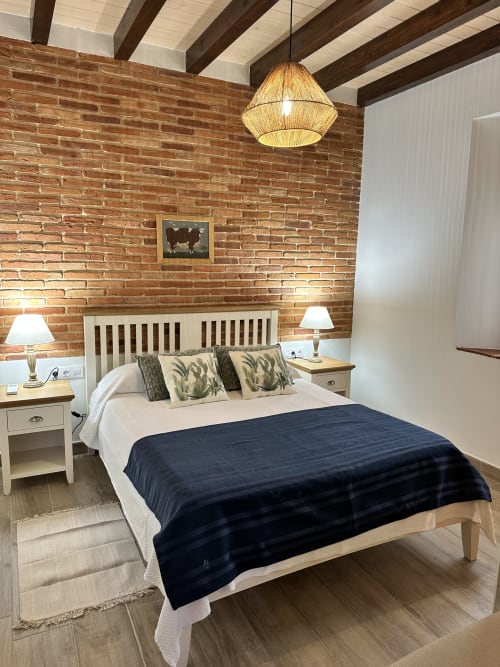 Acogedora habitación en El Escondite De Pedro Malillo con paredes de ladrillo, vigas de madera y ropa de cama azul marino en Candeleda