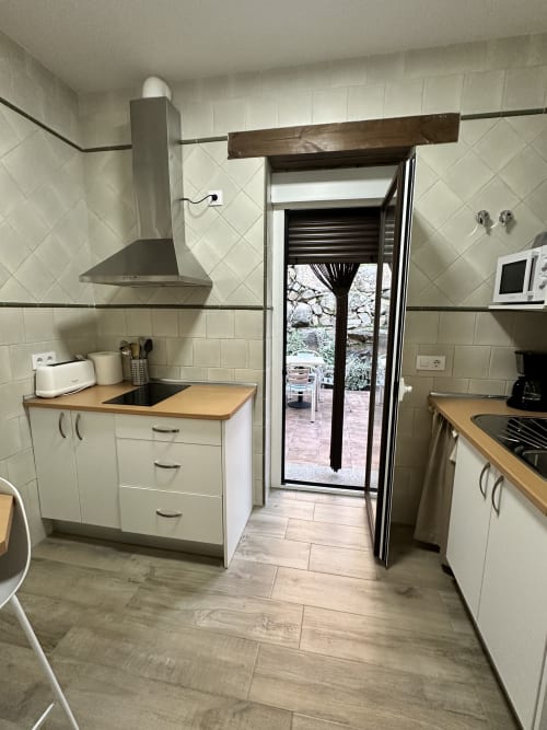Cocina moderna con muebles blancos, encimeras de madera, estufa de gas y puerta de vidrio hacia el patio de El Escondite De Pedro