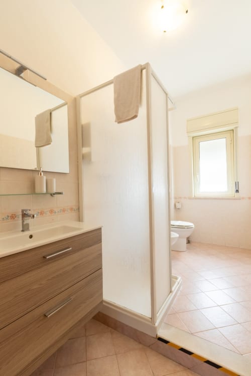 Bagno moderno presso La Zagara Rooms B&B a Milazzo con vanità in legno, doccia walk-in e pavimentazione in piastrelle beige