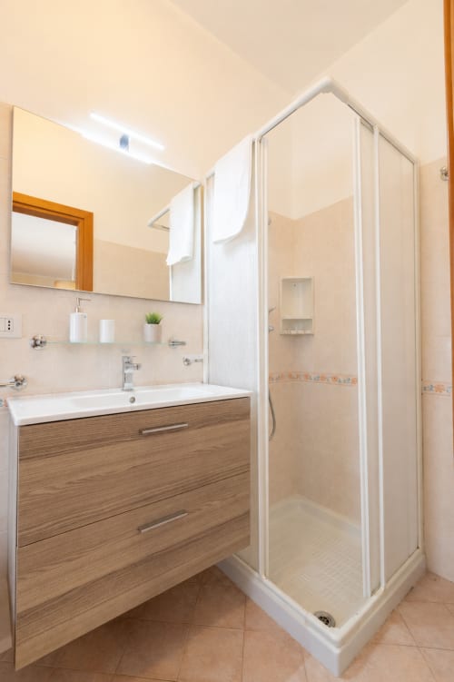 Bagno moderno presso La Zagara Rooms a Milazzo con mobile in legno, lavabo bianco, ampio specchio e box doccia in vetro