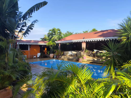 Guesthouse Villa Manguier à Rivière-Salée avec piscine bleue, plantes tropicales et terrasse couverte, bâtiment orange