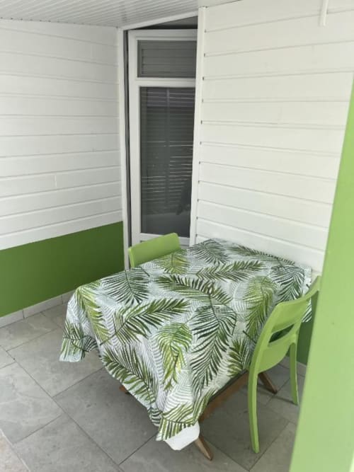 Espace de détente du bungalow Atoll avec fauteuils verts et nappe aux motifs de feuilles de palmier à la Résidence B&L Lagon