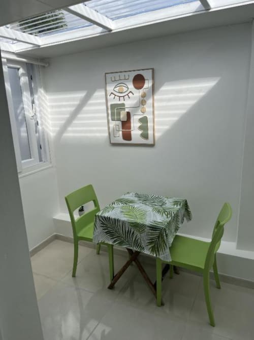 Chambre lumineuse à la Résidence B&L Lagon avec chaises vertes, nappe à motifs de feuilles de palmier, puits de lumière et art mural contemporain