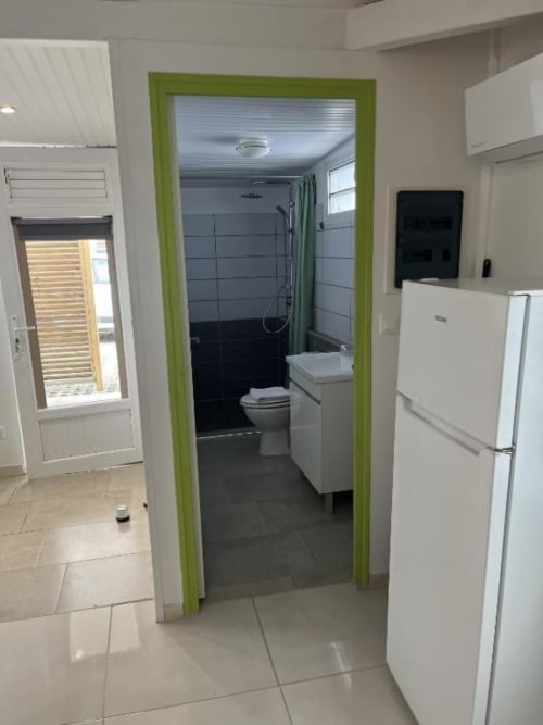 Entrée cuisine et salle de bain du bungalow Atoll à la Résidence B&L Lagon, avec électroménagers modernes et porte encadrée de vert