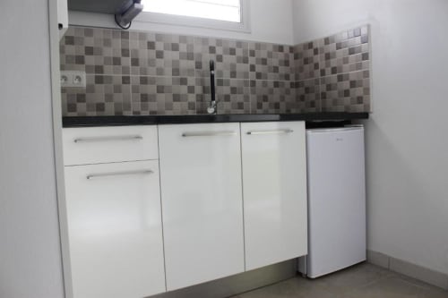 Petite kitchenette du bungalow à l'Atoll de la Résidence B&L Lagon : armoires blanches, plan de travail noir et crédence carrelée
