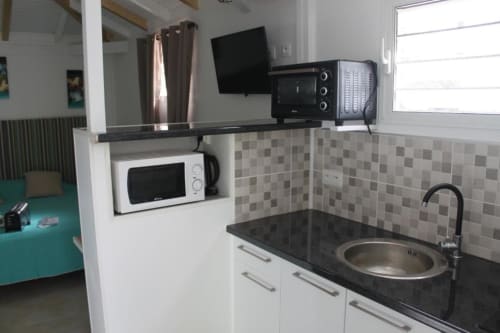 Kitchenette moderne au Bungalow Atoll de la Résidence B&L Lagon avec micro-ondes, cuisinière, évier et TV