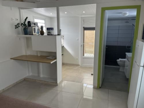 Kitchenette du bungalow Résidence B&L Lagon avec comptoir blanc, bar en bois et entrée de salle de bain encadrée de vert