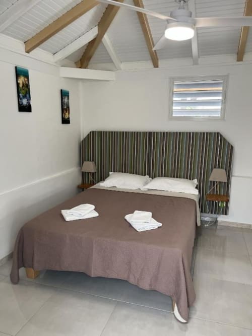 Chambre moderne du bungalow à la Résidence B&L Lagon avec lit queen-size, tête de lit rayée, plafond cathédrale et vue sur le jardin