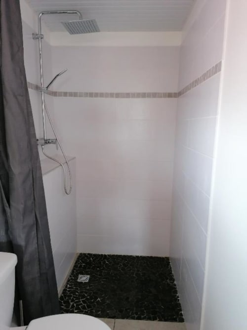 Douche moderne avec pommeau de pluie, douchette, carrelage noir mosaïque et murs blancs au Bungalow Corail
