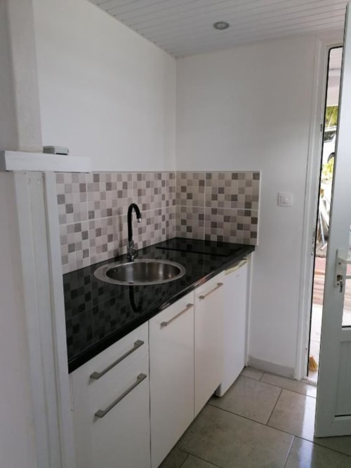 Kitchenette moderne du Bungalow Corail à la Résidence B&L Lagon avec plan de travail noir, évier rond et dosseret carrelé