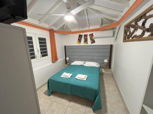 Chambre douillette du bungalow à la Résidence B&L Lagon avec literie turquoise, vue sur jardin et ventilateur plafond blanc
