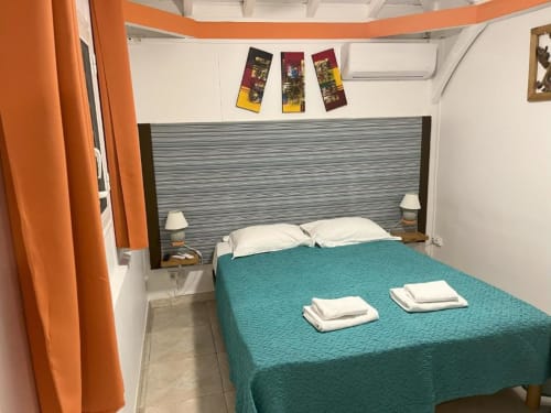 Chambre Bungalow Corail à la Résidence B&L Lagon avec lit turquoise, oreillers blancs, rideaux orange et tête de lit moderne