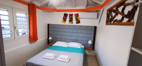 Chambre Bungalow Corail à la Résidence B&L Lagon avec literie turquoise, tête de lit rayée et rideaux orange