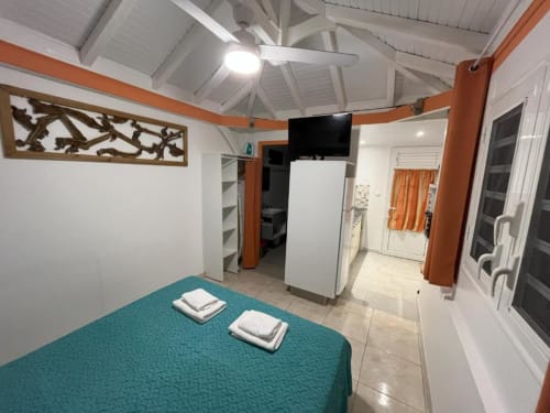 Chambre Bungalow Corail à la Résidence B&L Lagon en Martinique avec lit turquoise, ventilateur de plafond blanc et kitchenette
