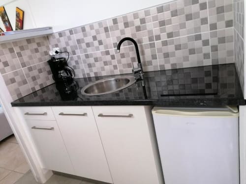 Kitchenette du bungalow Corail à la Résidence B&L Lagon avec plan de travail noir, armoires blanches et dosseret en mosaïque