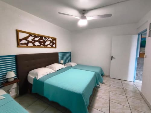 Chambre moderne à la Résidence B&L Lagon à Sainte-Luce avec literie turquoise, ventilateur de plafond et accès à la vue sur le jardin
