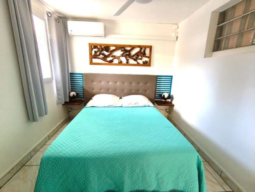 Chambre lumineuse à la Résidence B&L Lagon avec literie turquoise, tête de lit grise et décoration murale en bois à ce gîte de Sainte-Luce.