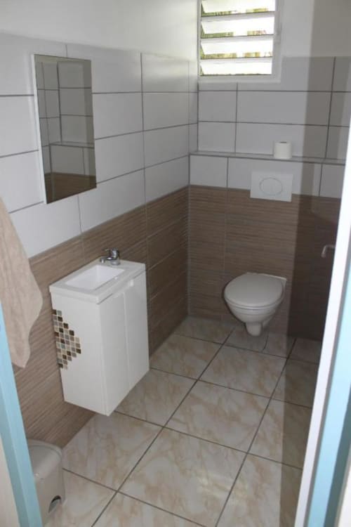 Salle de bain moderne de l'appartement Alisée à la Résidence B&L Lagon, Sainte-Luce avec toilettes, lavabo et carrelage imitation bois