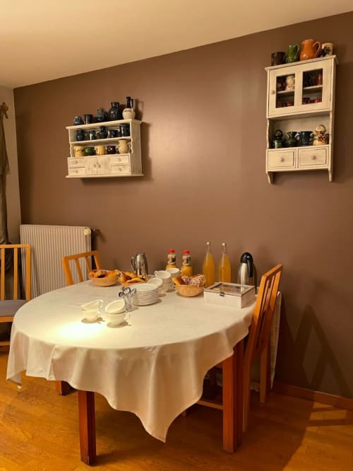 Élégante salle à manger de l'Au Bon Gîte avec table ronde, chaises en bois et étagères murales crème à Senones