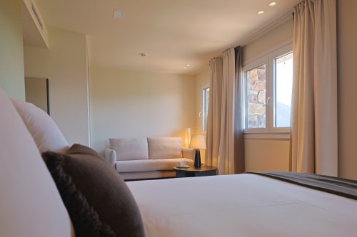 Deluxe double room at Hotel Fonsispa with bed, sofa, mountain views through balcony doors, and warm lighting