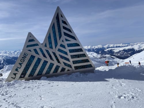 Le lodge géométrique L'Alp'In dans les montagnes enneigées de La Plagne avec pics alpins et skieurs