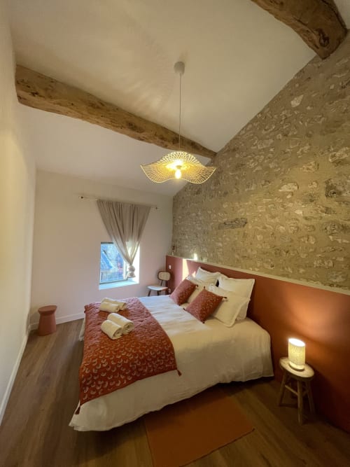 Chambre douillette au Domaine Maison Girardon avec poutres apparentes, mur en pierre et éclairage chaleureux à La Roche-sur-Grane
