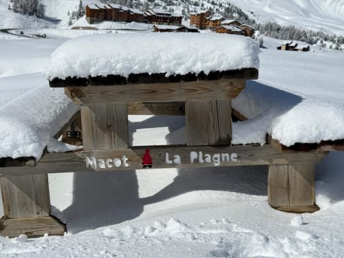 Banc mascotte enneigé en bois à L'Alp'In à La Plagne, station alpine avec chalets en arrière-plan