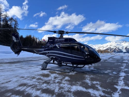 Hélicoptère Jet Systems sur un héliport enneigé avec vue sur L'Alp'In, massif de la Plagne Tarentaise en arrière-plan