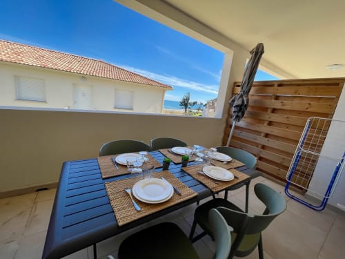 Seaside terrace dining at Marina di Bravone with set table, ocean view, wooden privacy screen and covered seating
