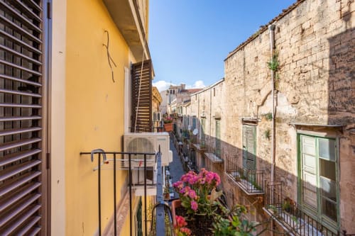 Balconata con vista sulla storica strada di Palermo con edifici colorati e fiori rosa dell'hotel Marilù