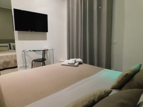 Camera doppia moderna al Marilù B&B di Palermo con TV a parete, scrivania e vista sulla città attraverso le tende