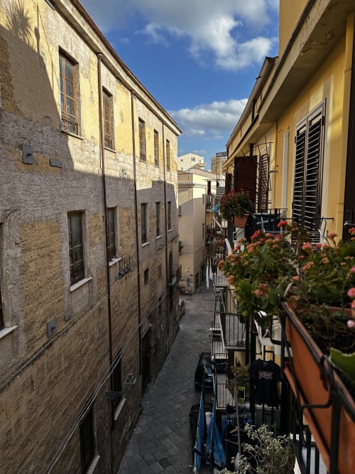Vicolo stretto di Palermo con edifici storici in pietra, fiori colorati e persiane tradizionali al Marilù B&B