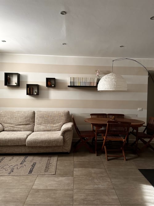 Lounge Marilù Palermo BnB con divano color crema, tavolo in legno, pareti rigate e scaffali sospesi