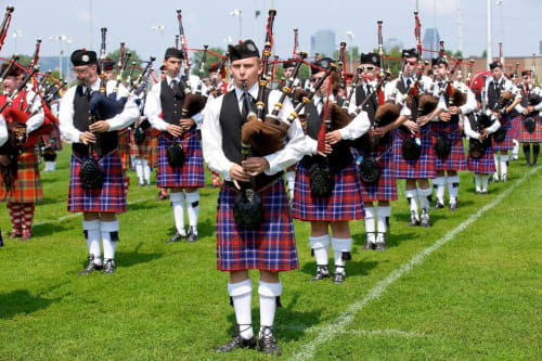 Scottish bagpipe band in kilts performing on grass field near Perth, GB