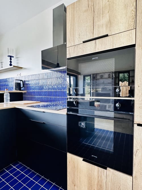 Cuisine moderne du cottage L'Instant à Vivre l'Instant, Amboise, avec mobilier noir, dosseret carrelage bleu et accents bois