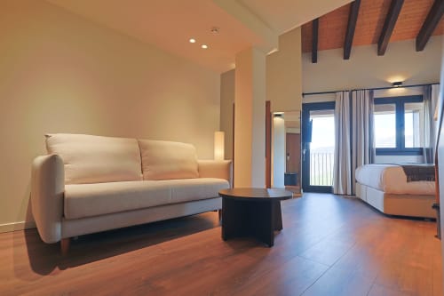 Modern hotel suite at Hotel Fonsispa in Renanué with cream sofa, wooden beams, and bed visible through glass doors