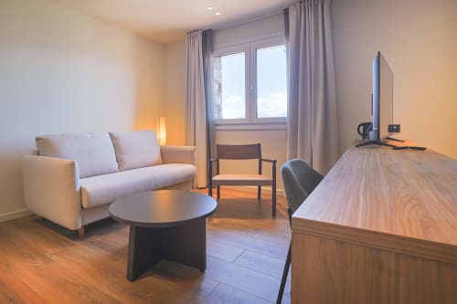 Modern hotel room at Hotel Fonsispa in Renanué with sofa, desk, TV, and large window with curtains