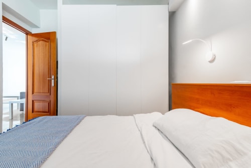 Modernes Schlafzimmer mit orangefarbenem Holzkopfteil, weißer Bettwäsche und reichlich natürlichem Licht in der M&M Suite Yumbo Atlantis Wohnung