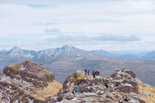 Hikers on rocky mountain peaks with snow-capped mountains and valleys in background