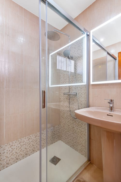 Modernes Badezimmer mit Glasduschkabine, Regenschauer-Duschkopf, beleuchtetem Spiegel und beigefarbigen Fliesen in der M&M Suite Yumbo