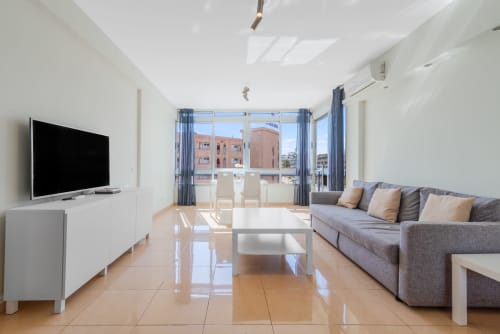 Helles modernes Apartment in Maspalomas mit Wohnzimmer, Sofa, TV, weißem Couchtisch und Balkonblick auf rosa Gebäude