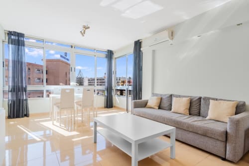 Helles modernes Apartment in Maspalomas mit Terrasse, grauem Sofa, Esstisch und bodentiefen Fenstern