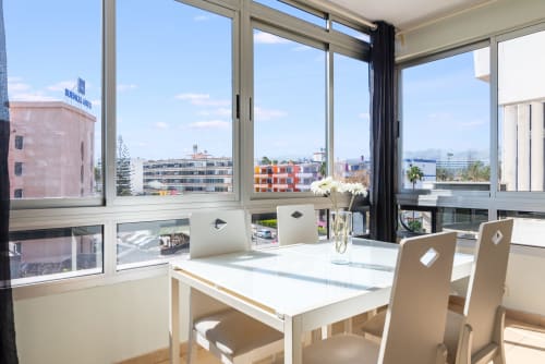 Helles Esszimmer mit raumhohen Fenstern mit Blick auf den Maspalomas-Pool und die Stadtaussicht, weißer Tisch in Beige-Tönen