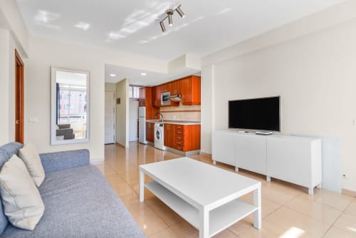 Modernes Wohnzimmer und Küche in Maspalomas mit TV, weißen Möbeln, orangefarbigen Schränken und Poolblick