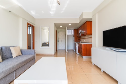 Modernes Wohnzimmer einer Apartment mit grauem Sofa, weißem Tisch, Fernseher und Küche mit Holzschränken in Maspalomas
